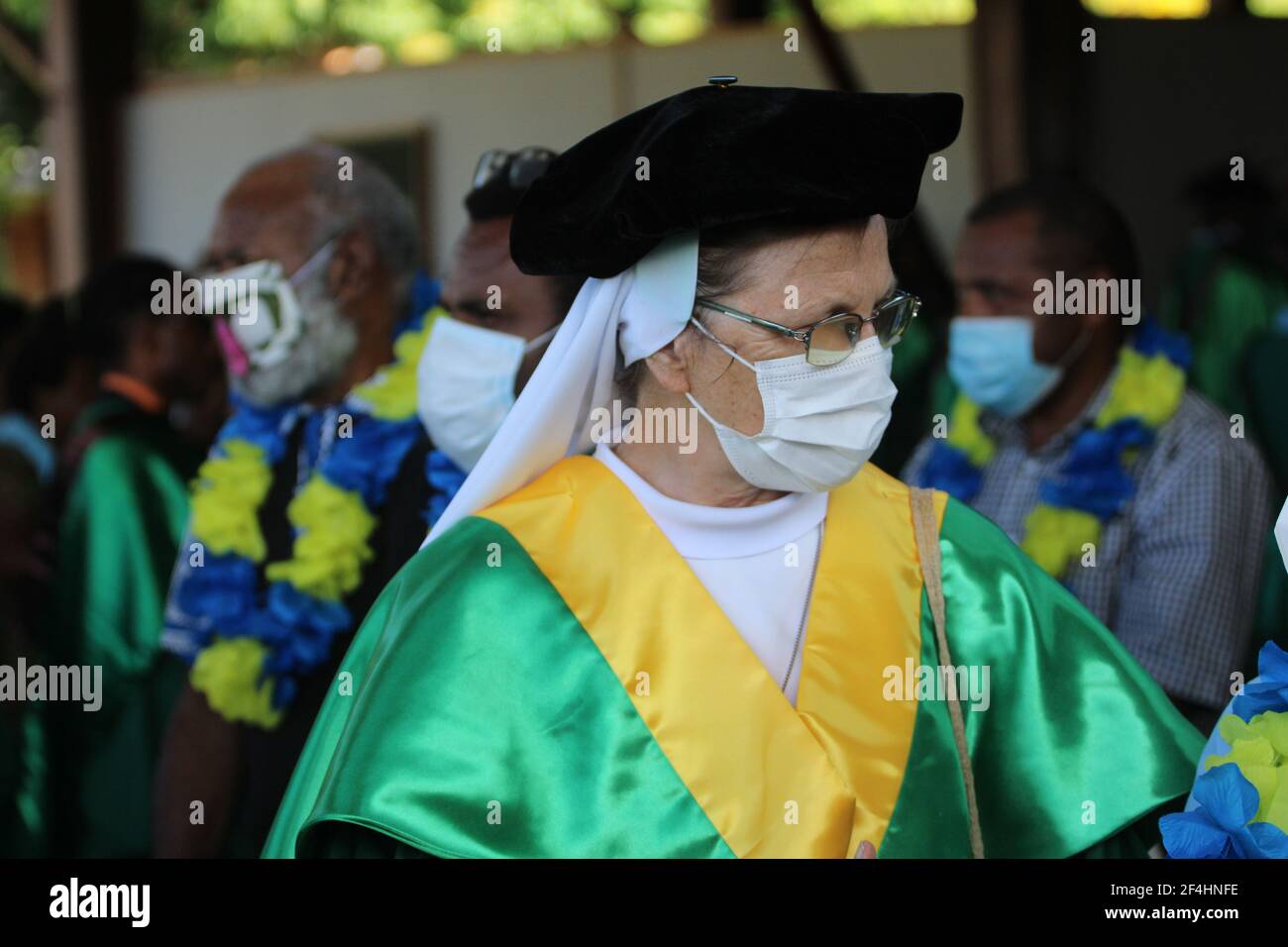 Cérémonie de remise des diplômes de l'université au DWU avec le personnel académique portant des regalia vertes et jaunes, des masques faciaux et des vêtements de convocation traditionnels Banque D'Images
