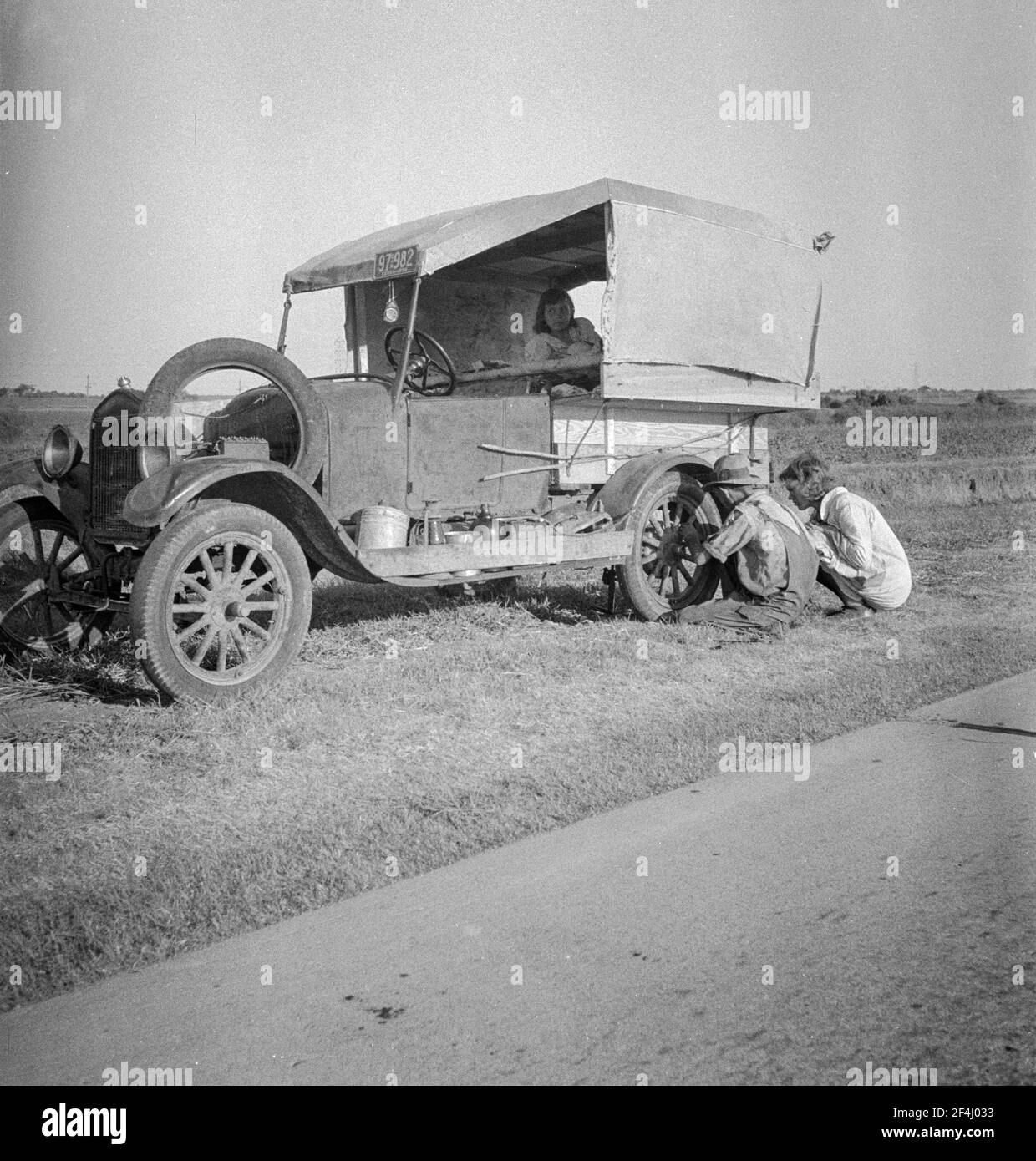 Famille entre Dallas et Austin, Texas. Les gens ont quitté leur maison et leurs connexions dans le sud du Texas, et espèrent atteindre le delta de l'Arkansas pour le travail dans les champs de coton. Personnes sans pénitence. Pas de nourriture et trois gallons de gaz dans le réservoir. Le père tente de réparer un pneu. Trois enfants. Le père dit: «c'est dur, mais la vie est dure de toute façon que vous le prenez». Août 1936. Photo de Dorothea Lange. Banque D'Images