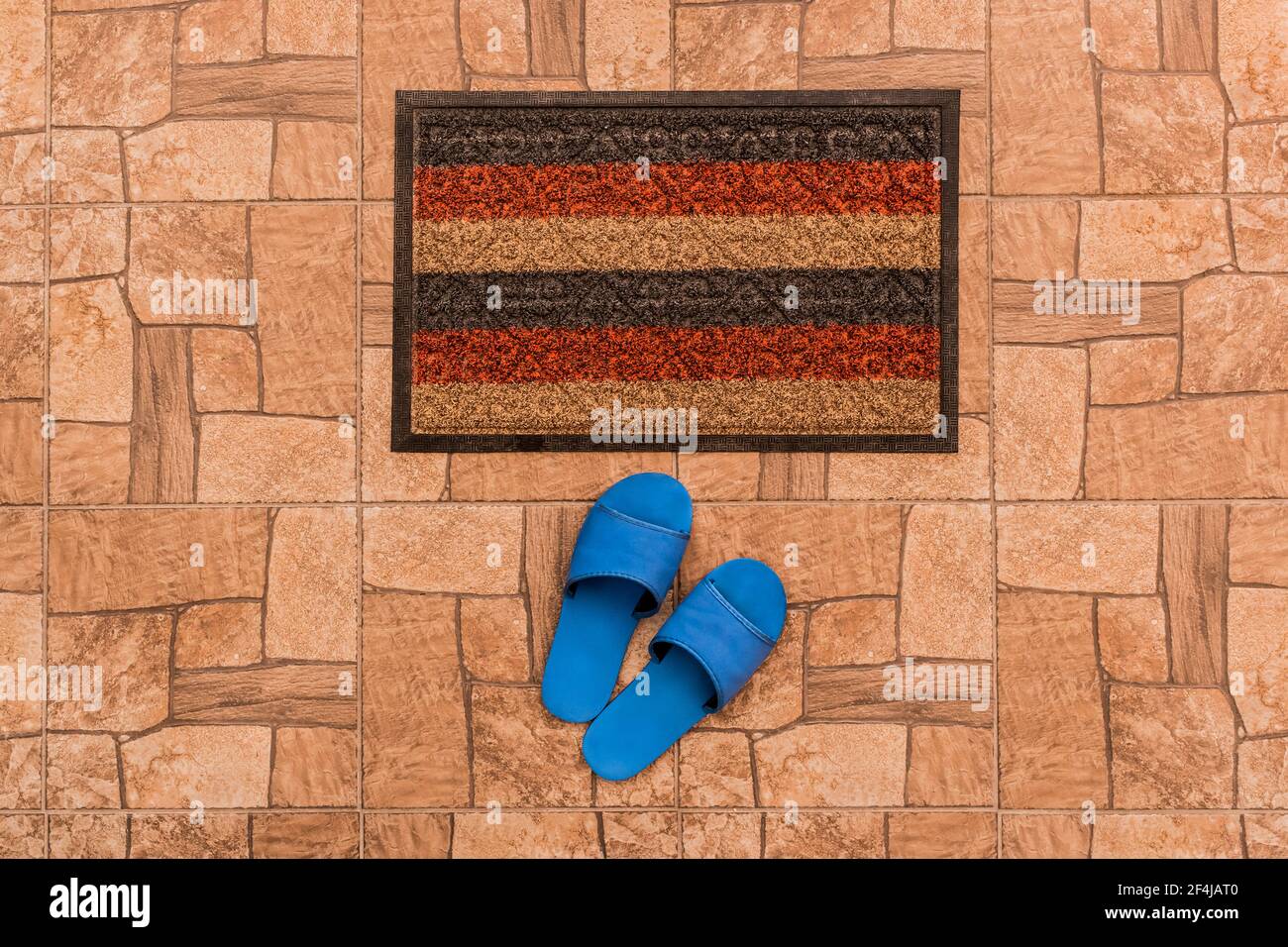 Les pantoufles maison bleues pour hommes se tiennent près du tapis de pied sur un fond de sol carrelé marron texturé, vue du dessus. Banque D'Images
