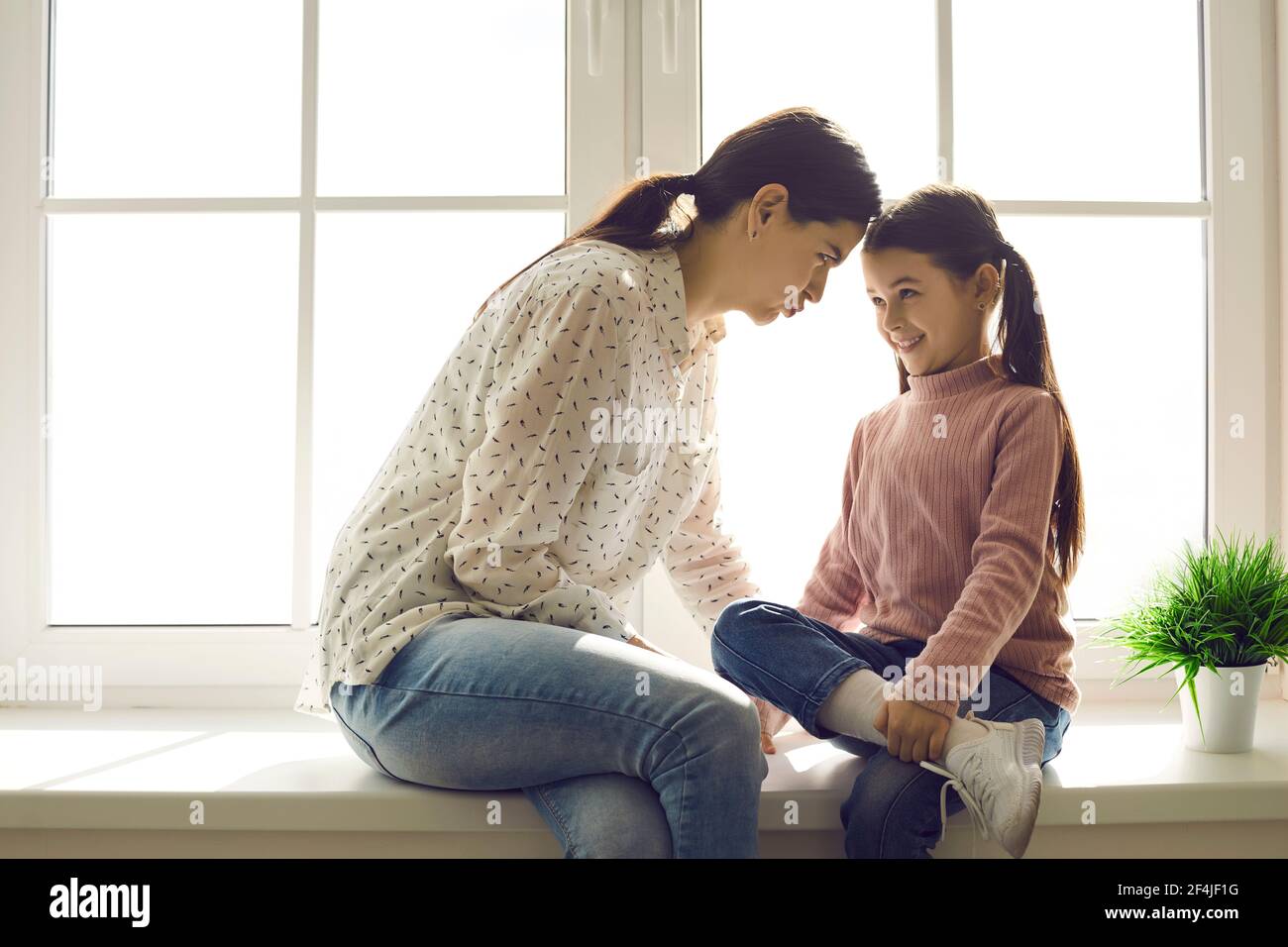 Bonne maman et enfant assis sur le rebord de la fenêtre, regardant les uns les autres et faisant des visages drôles Banque D'Images