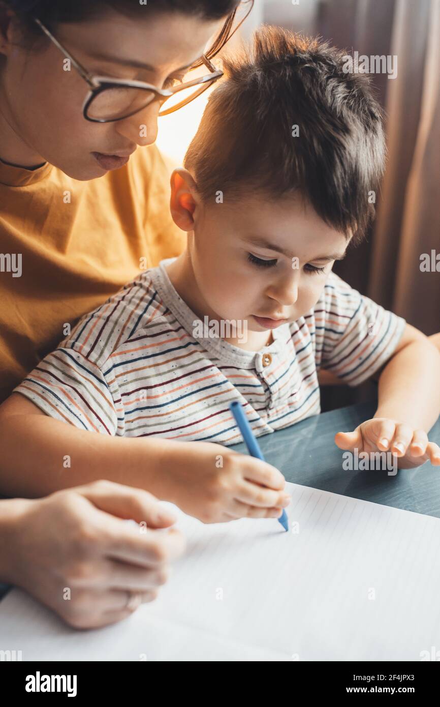 Gros plan d'une mère de race blanche avec des verres aidant son fils pour faire ses devoirs Banque D'Images