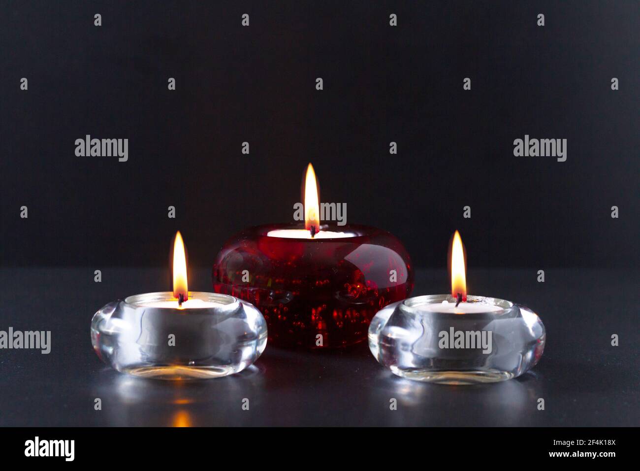 Concept de deuil ou de prière. Trois bougies allumées sur fond noir. Deux  d'entre eux en chandeliers en verre transparent et un en lustre en verre  rouge Photo Stock - Alamy
