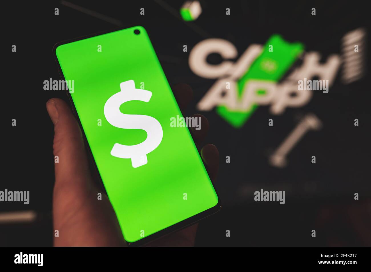 Homme tenant un smartphone avec le logo vert de l'application Cash dollar icône avec site web flou comme arrière-plan Banque D'Images