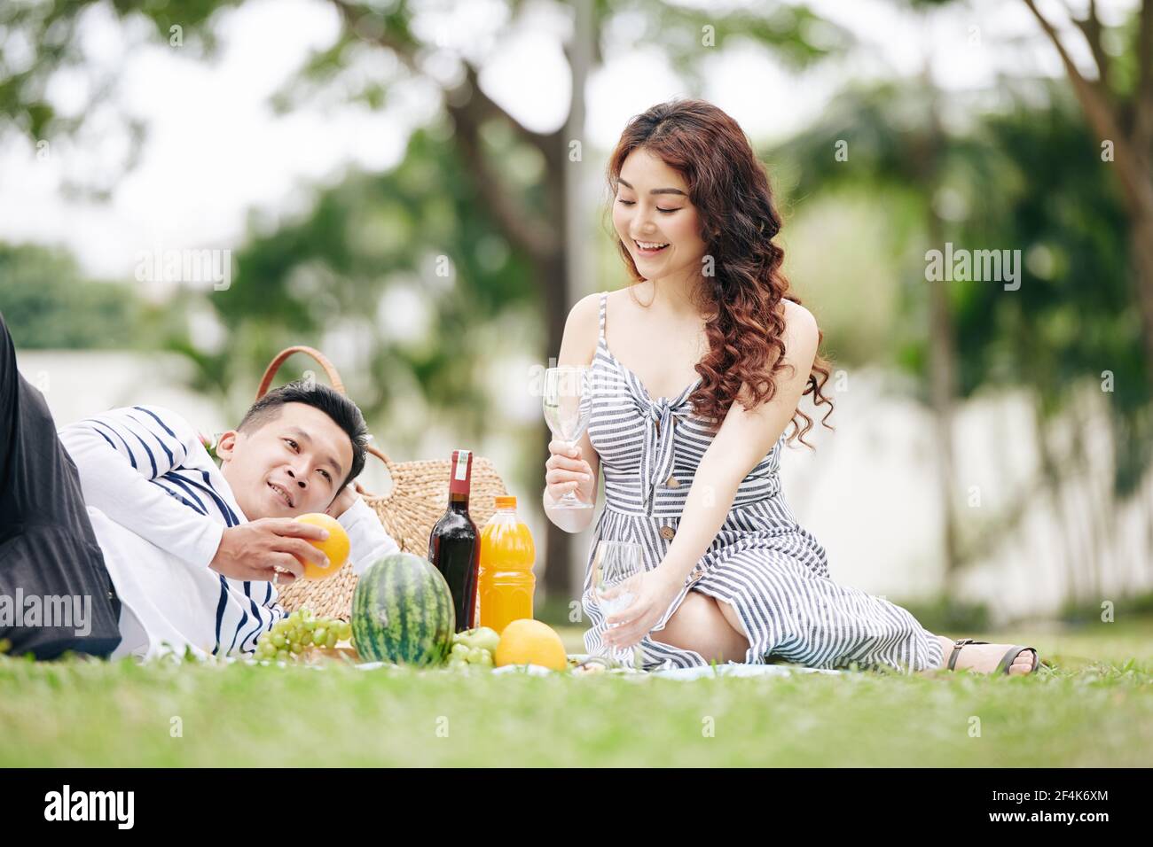 Joyeux jeune couple asiatique amoureux de boire du vin et de manger fruits lors d'un pique-nique dans le parc Banque D'Images
