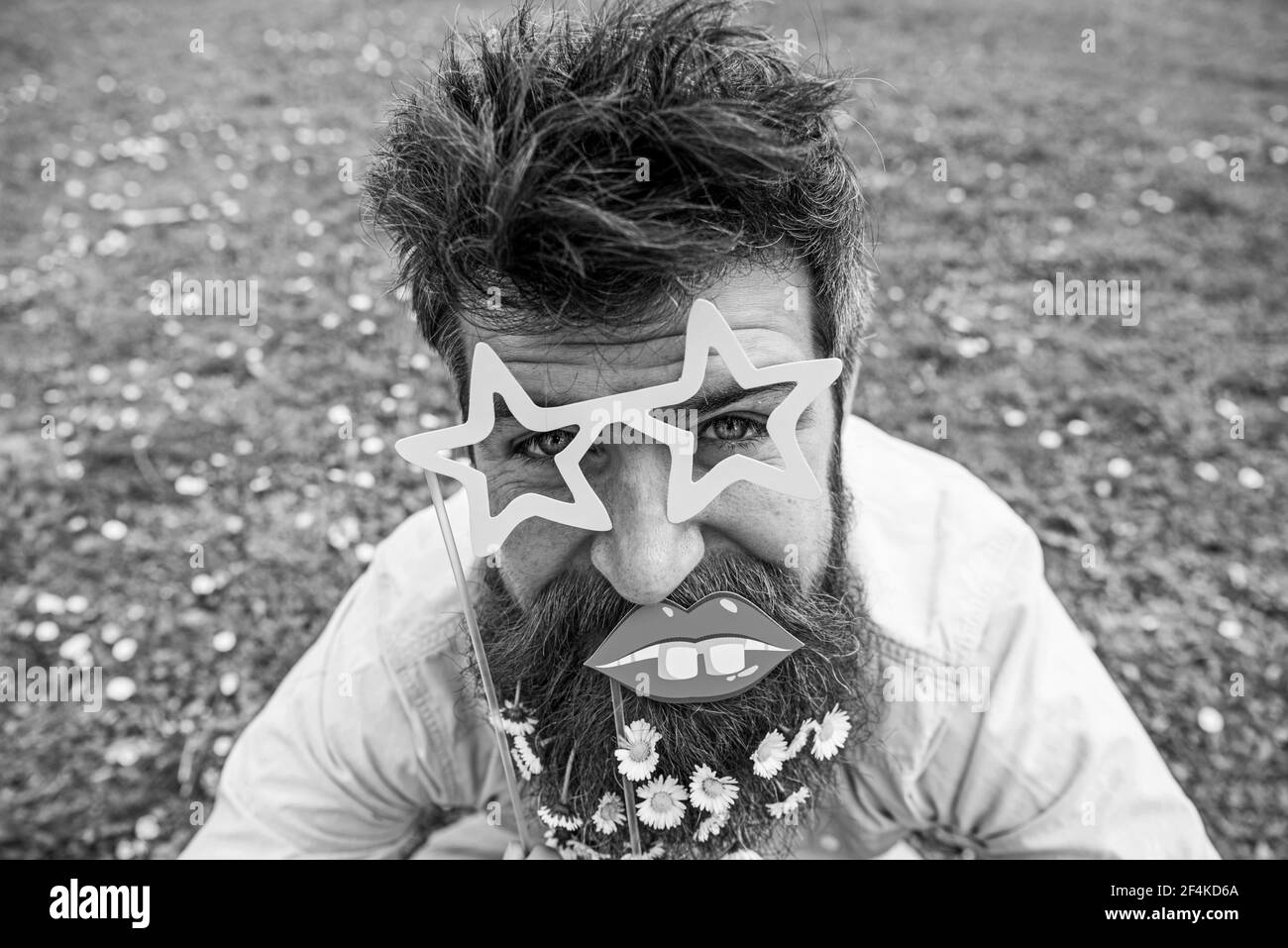 Concept de photosession. Taille basse avec barbe sur le visage gai, posant avec des verres et des lèvres en forme d'étoile. Guy est joliment décoré de fleurs de pâquerette. Homme Banque D'Images