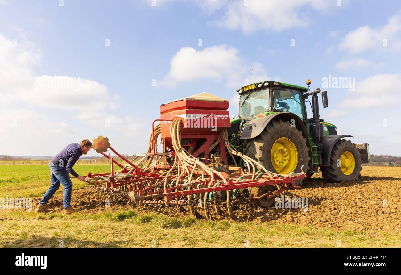 Agriculteur vérifiant une machine d'ensemencement fixée à un tracteur au printemps. Hertfordshire. ROYAUME-UNI Banque D'Images