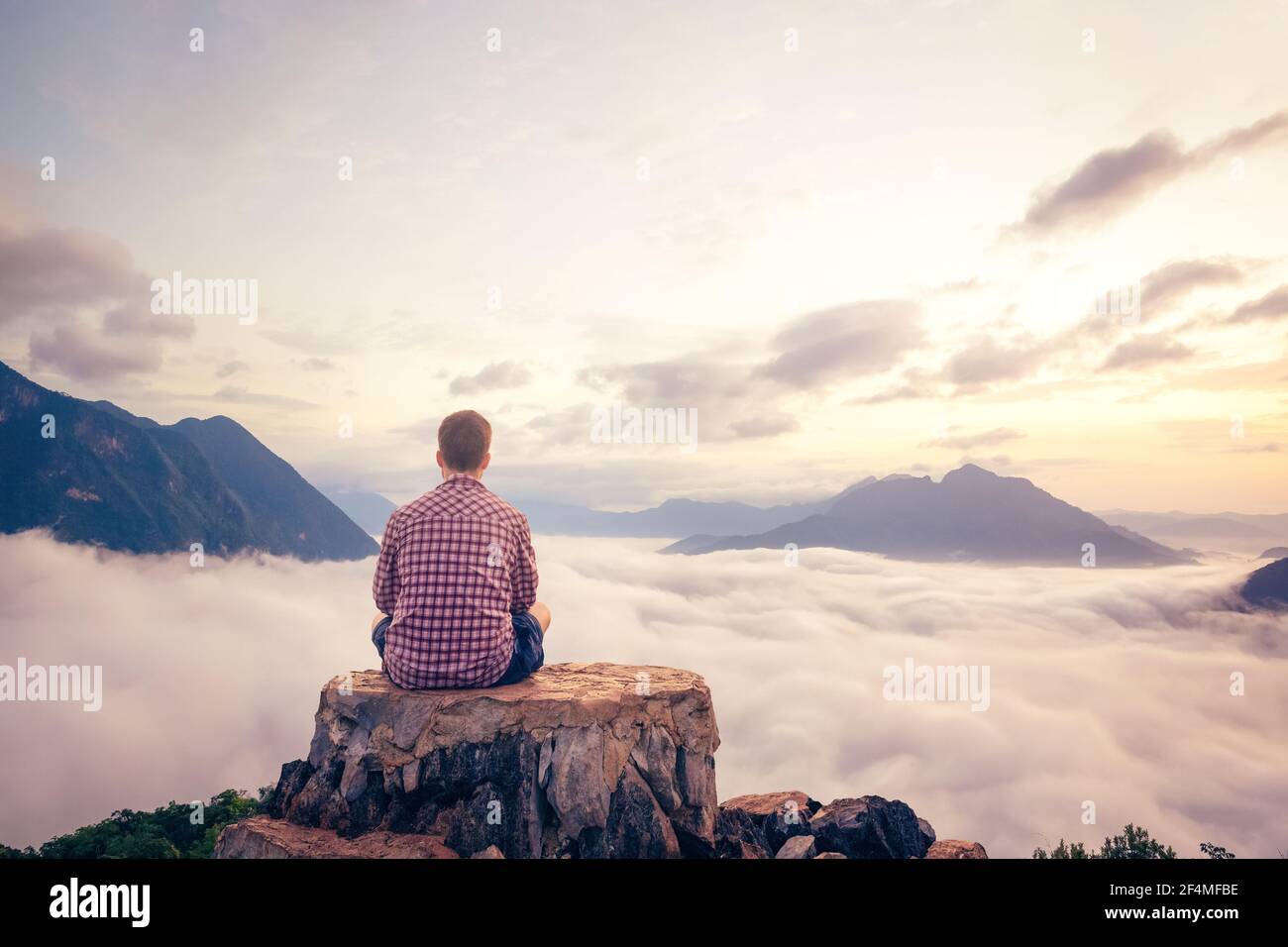 Homme assis sur un sommet avec une vue magnifique sur les nuages Banque D'Images