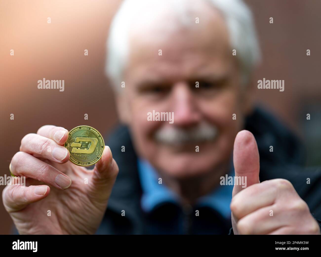 Symbole de Dash comme investissement dans un régime de retraite. Vieil homme tenant une pièce de monnaie du tableau de bord. Banque D'Images