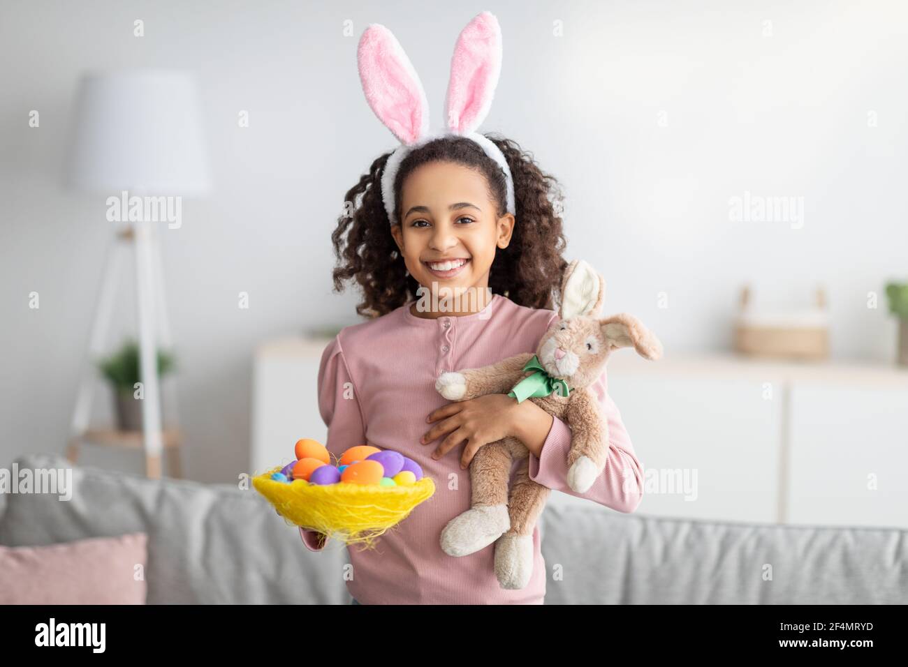 Mignon lapin de Pâques. Bonne fille noire tenant des œufs colorés lumineux dans un nid décoratif Banque D'Images