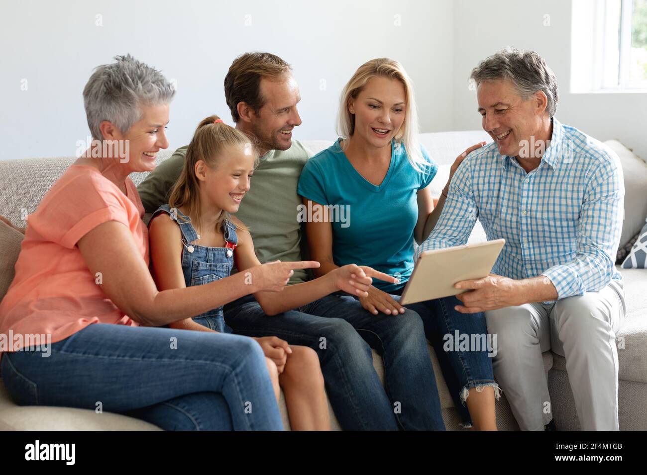 Grand-parents caucasiens souriants sur le canapé avec la petite-fille et ses parents regarder une tablette Banque D'Images