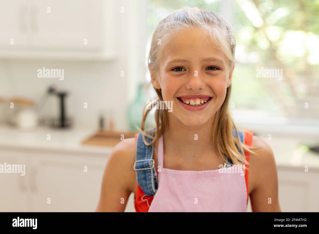 Portrait d'une fille caucasienne souriante portant un tablier debout dans la cuisine Banque D'Images