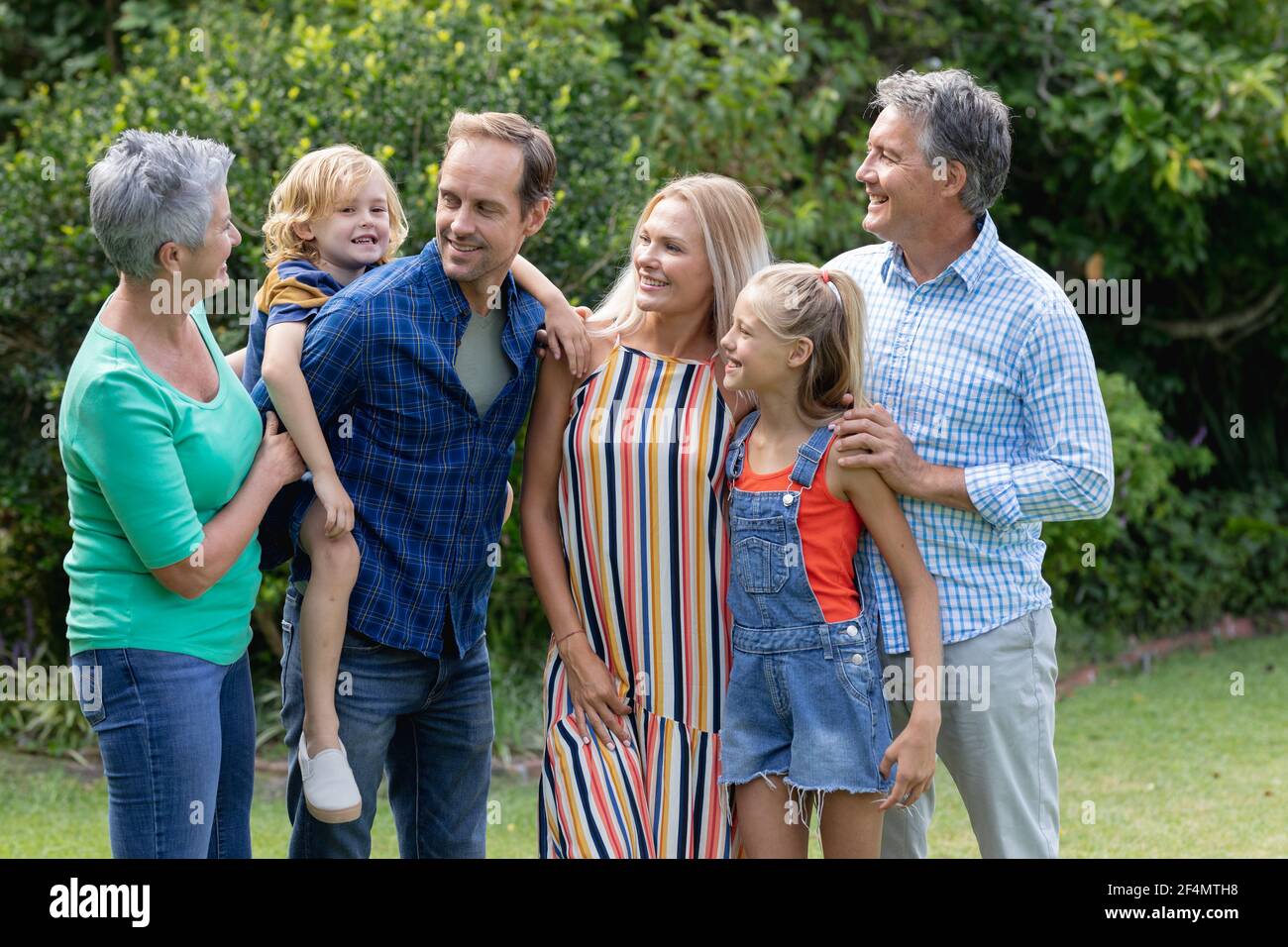 Parents, grands-parents et petits-enfants de race blanche debout dans un jardin qui parle et embrasse Banque D'Images