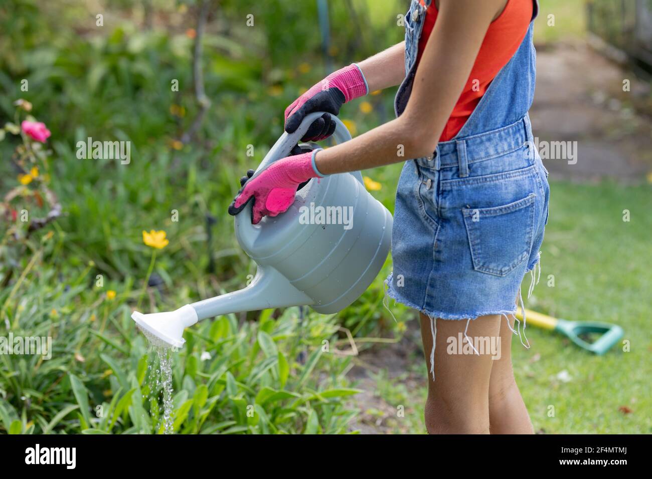 Section médiane de la fille caucasienne dans le jardin portant des gants et arrosoir plantes avec arrosoir Banque D'Images