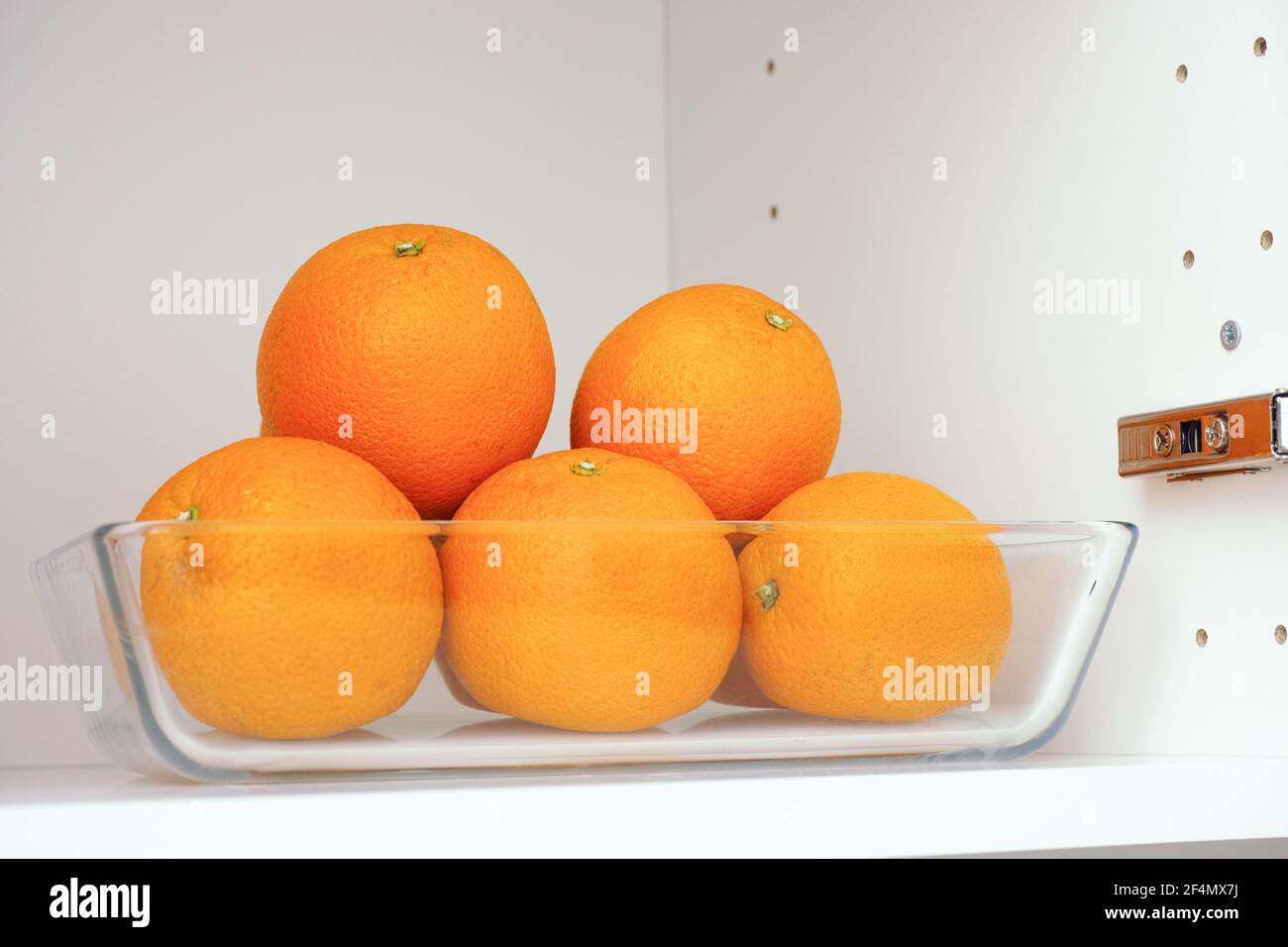 Oranges organiques dans un récipient en verre qui se trouve dans un placard de cuisine. Gros plan. Banque D'Images