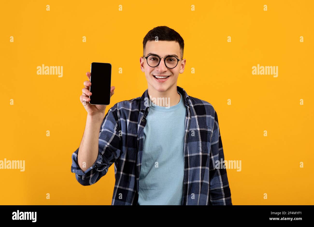 Portrait d'un jeune homme cool montrant un smartphone avec écran vide sur fond orange studio, maquette pour le design Banque D'Images