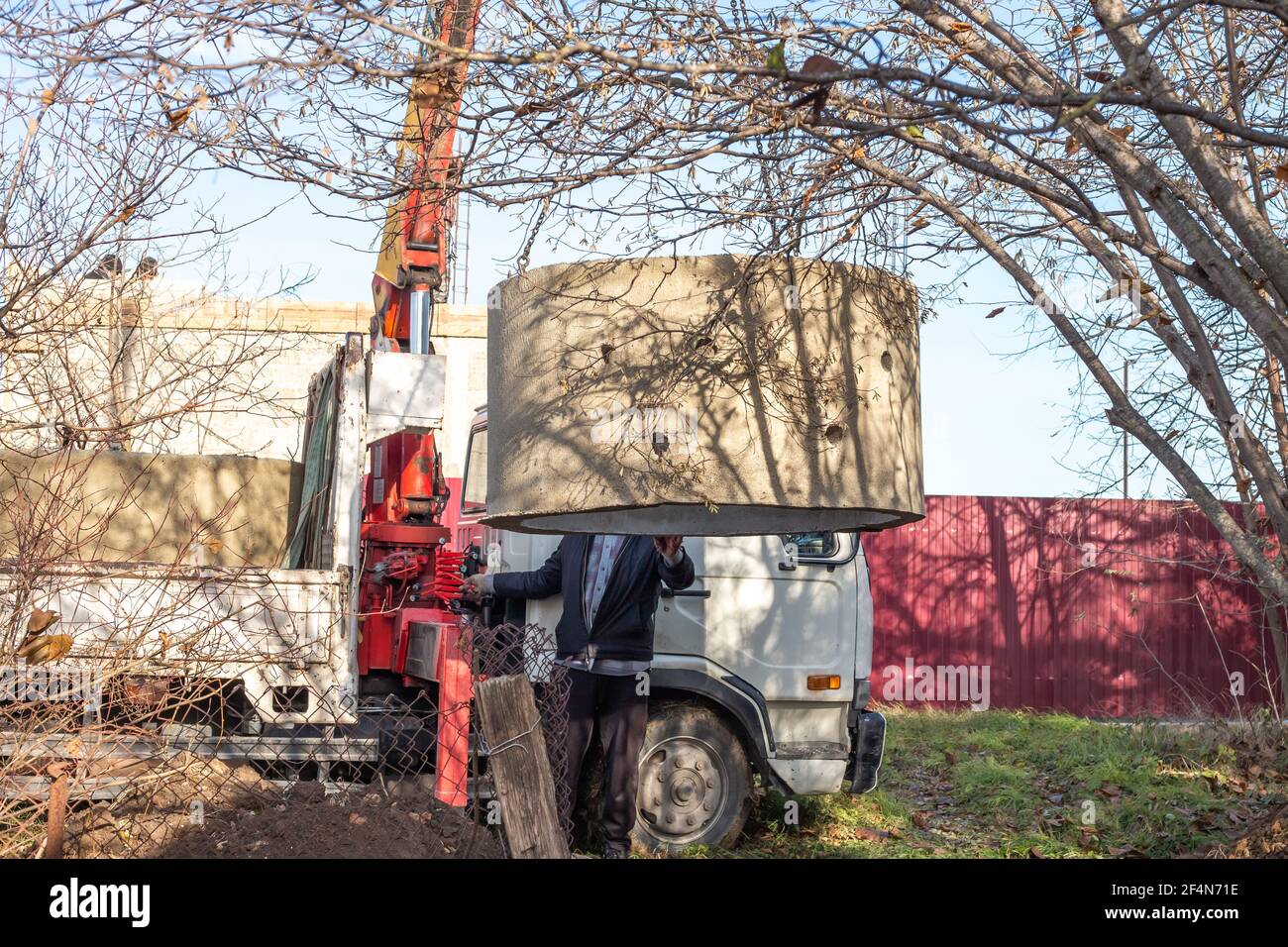 Déchargement par un chargeur d'un anneau en béton d'un diamètre de un mètre et demi dans un trou creusé pour la construction d'une fosse septique. Installation Banque D'Images