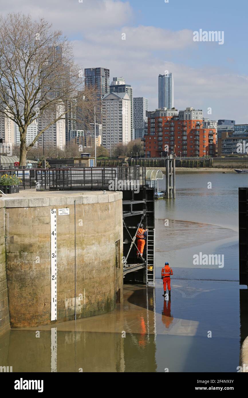 Deux ingénieurs travaillent à marée basse sur les écluses situées entre le quai du Groenland et la Tamise, à Rotherhithe, Londres, au Royaume-Uni. Canary Wharf en arrière-plan. Banque D'Images