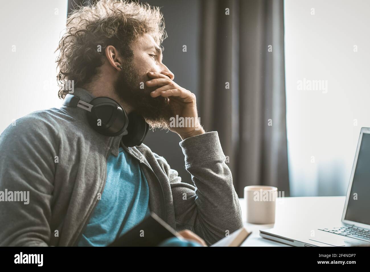 Un jeune entrepreneur diminue la comptabilité. L'homme prend des notes dans un bloc-notes et regarde l'écran de l'ordinateur assis à son bureau. Banque D'Images