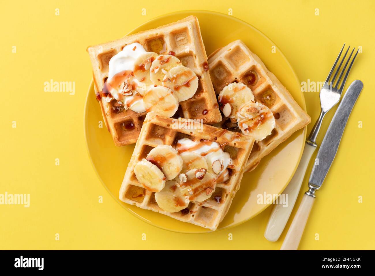 Gaufres belges avec banane, sauce caramel et amandes sur plaque jaune, fond jaune. Vue de dessus. Petit déjeuner sucré avec gaufres à la banane Banque D'Images