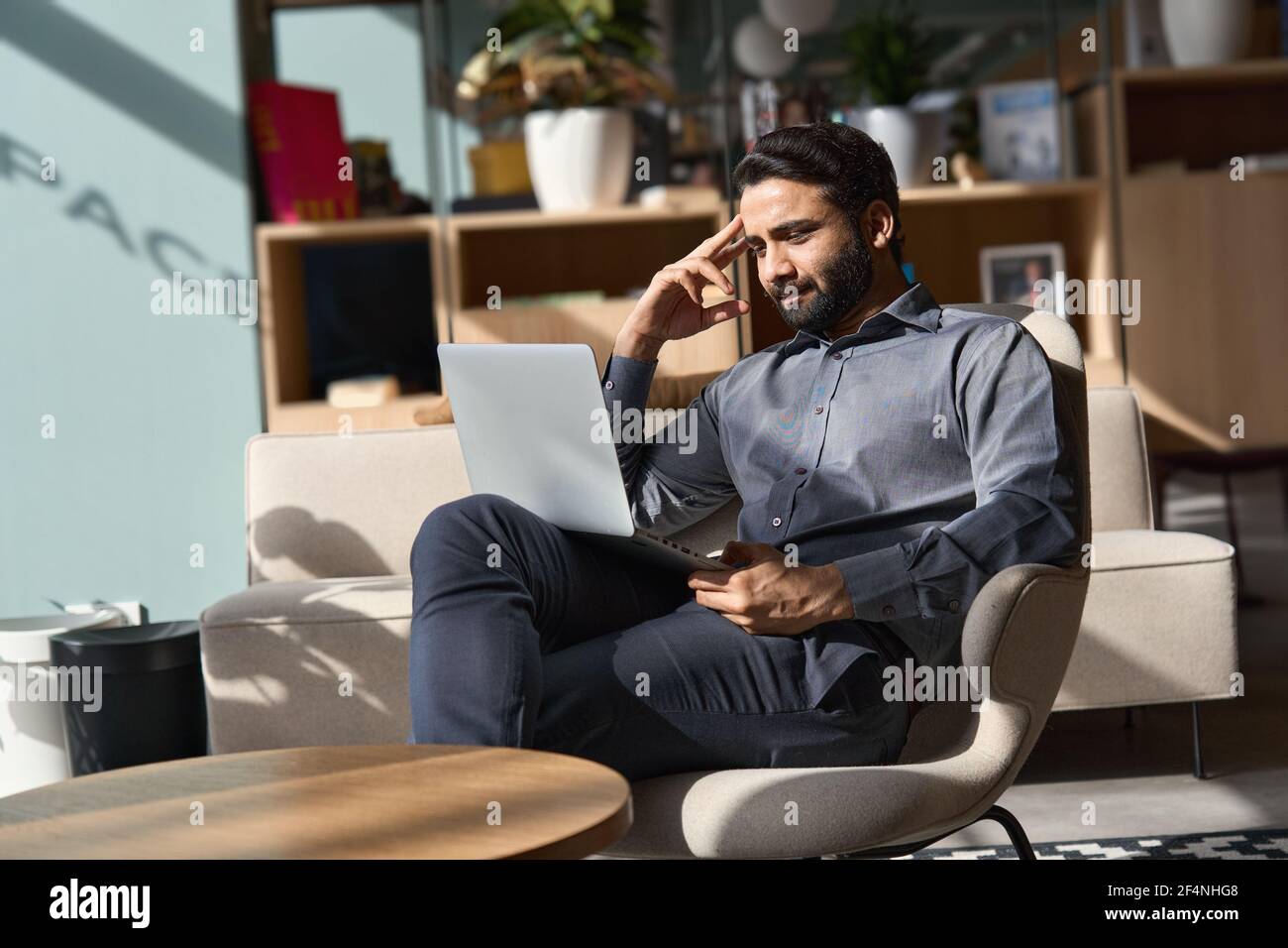 Un homme d'affaires indien travaillant sur un ordinateur portable, assis sur une chaise dans le bureau. Banque D'Images