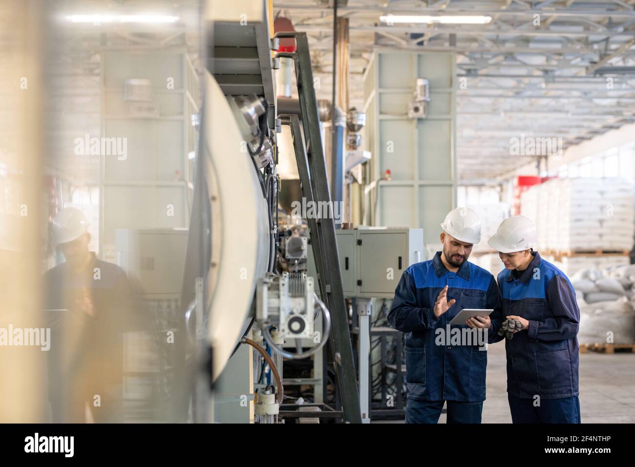 Deux jeunes travailleurs contemporains de l'usine moderne discutant technique en ligne données ou croquis des détails des machines industrielles en atelier Banque D'Images