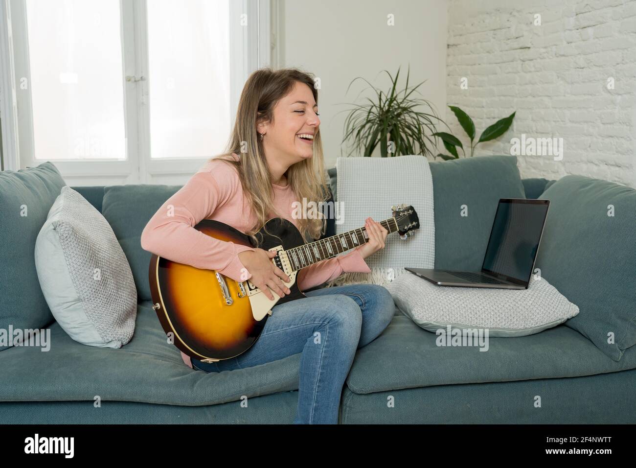 Femme jouant de la guitare électrique avec un ordinateur portable dans la leçon de musique en ligne. Femme s'amusant à regarder un didacticiel vidéo sur l'apprentissage de chansons rock. Loisirs et loisirs Banque D'Images
