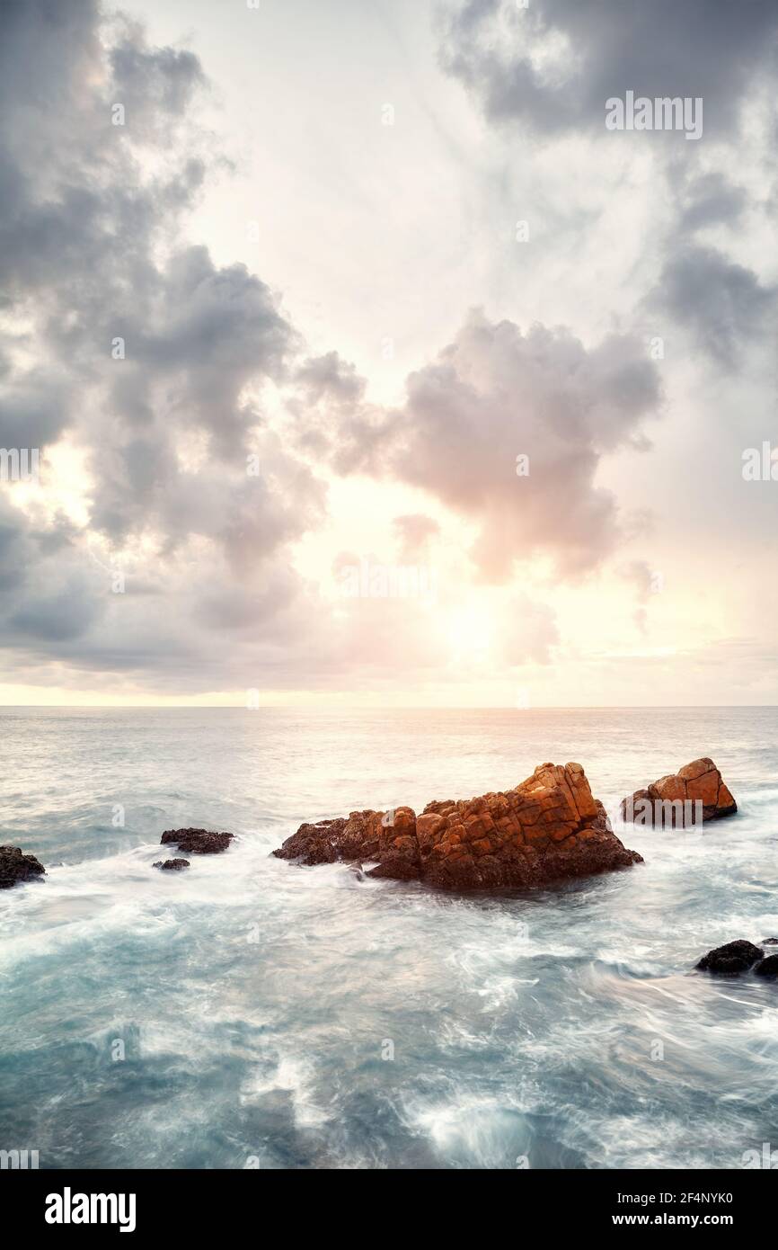 Rochers dans une mer au coucher du soleil, image de longue exposition. Banque D'Images