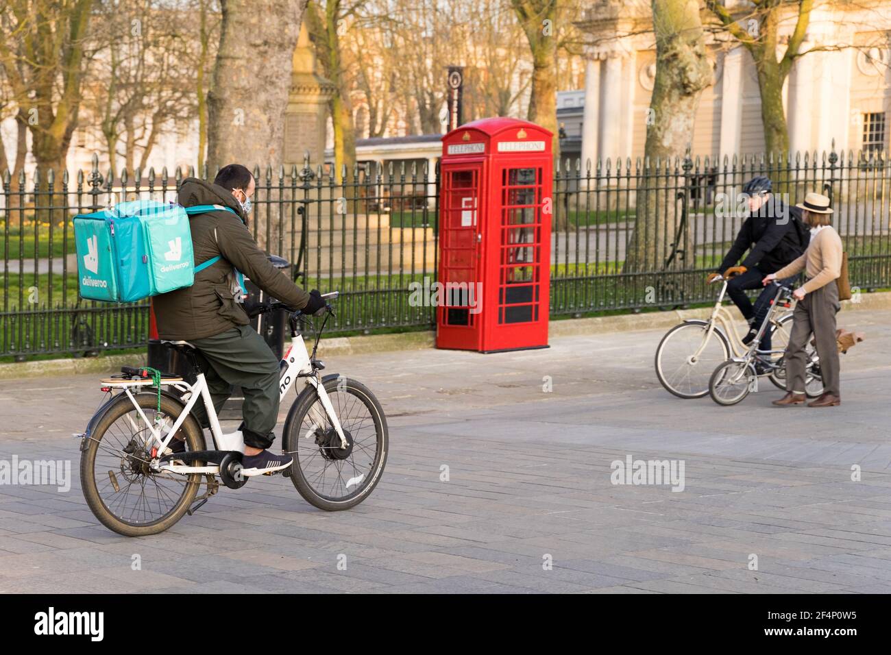 Deliveroo homme sur son vélo de coursier sur son chemin à emporter client, téléphone rouge boîte et deux autres cyclistes, Londres Greenwich Angleterre Banque D'Images