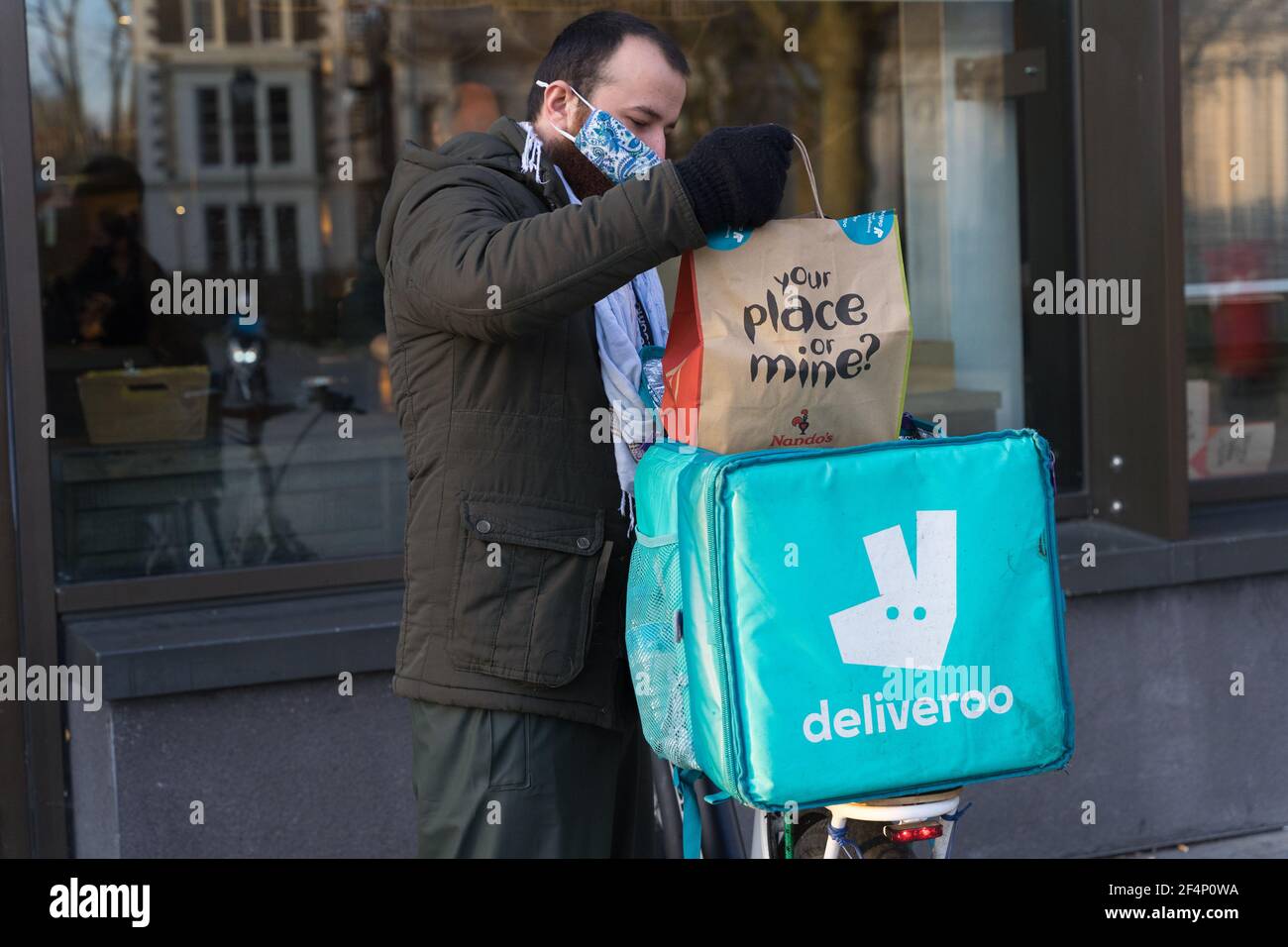 Delvieroo homme portant un masque de visage met la nourriture à emporter de Nando's dans le sac arrière ajusté à son vélo, Londres, Angleterre Banque D'Images