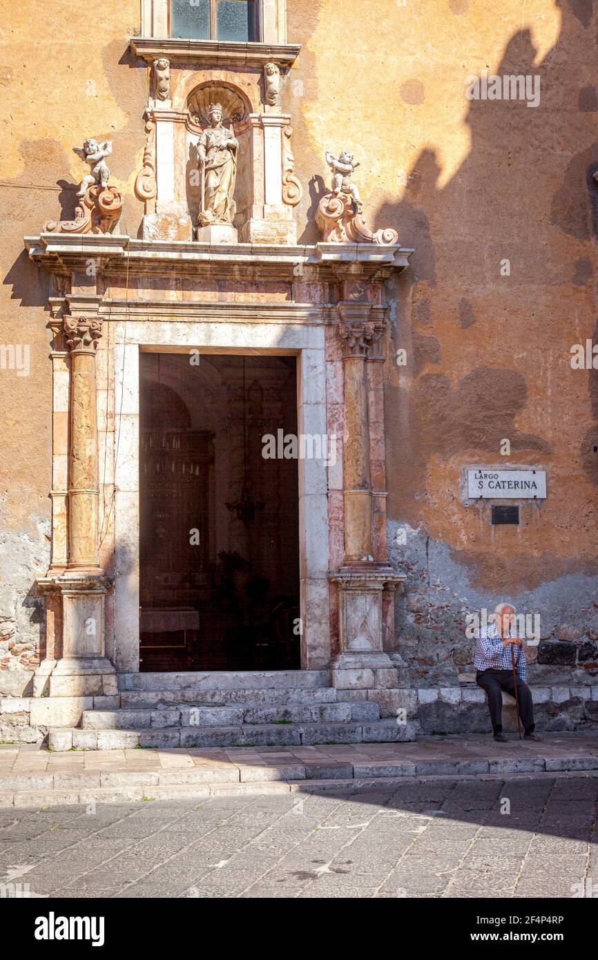 Homme plus âgé assis à la porte d'entrée de Chiesa di Santa Caterina (b. 1610) à Taormina, Sicile, Italie Banque D'Images