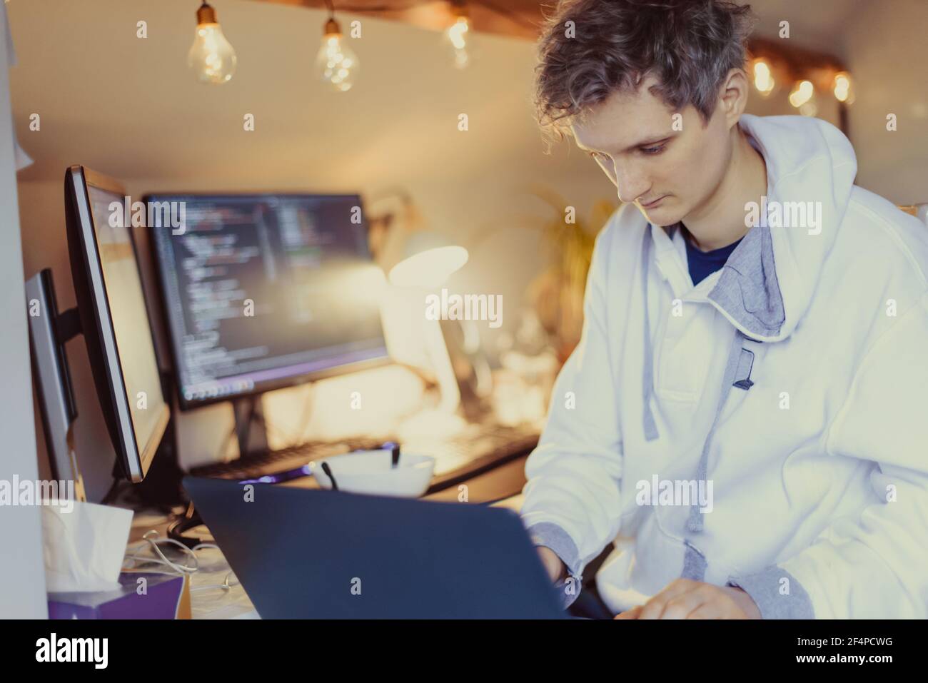 Un homme assis à un bureau travaillant à la maison sur son ordinateur. Un programmeur informatique spécialisé écrit du code sur son pc et son ordinateur portable. Bureau à distance du développeur Banque D'Images