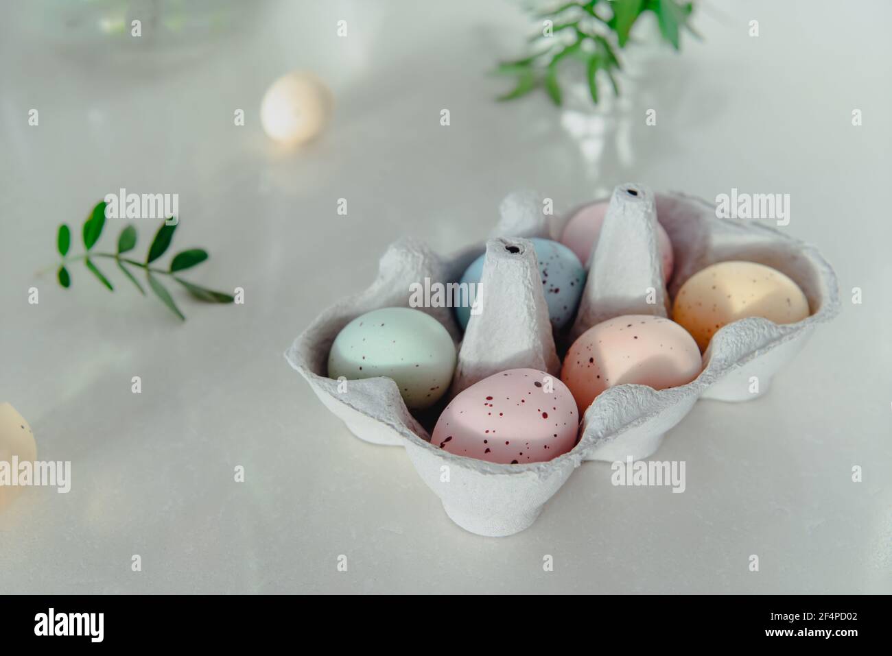 Concept de vacances de Pâques. Les couleurs pastel ont peint les œufs dans une boîte en carton et avec de petites feuilles vertes fraîches sur fond blanc. Lumière naturelle douce. Festif Banque D'Images