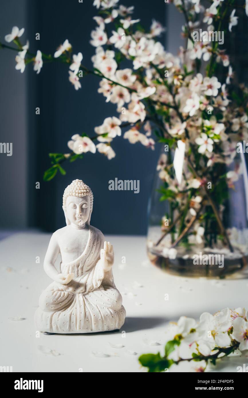 Statuette de Bouddha blanc décorative avec branches d'arbre en forme de sang dans le vase sur fond sombre. Méditation et rituel de relaxation. Anniversaire de Bouddha Banque D'Images