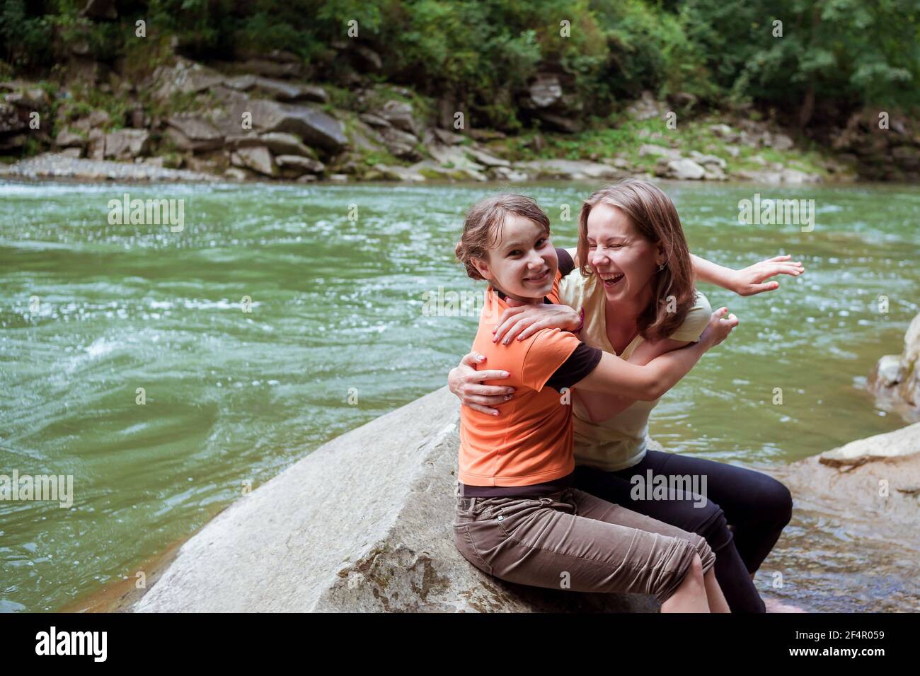 Deux filles embrassant et souriant sur la grande pierre dedans forêt en face de la rivière Banque D'Images