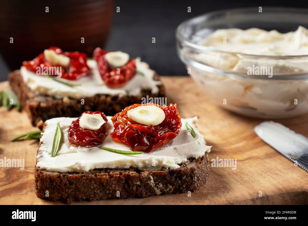 Petits-sandwiches multigrains faits maison avec fromage à la crème et tomates séchées sur un plateau en bois, gros plan. Concept de saine alimentation Banque D'Images