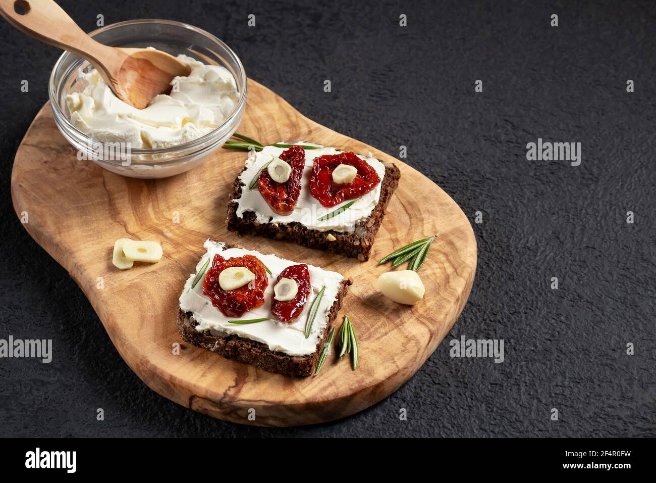 Des sandwichs au pain multigrain faits maison avec fromage à la crème et tomates séchées sur un plateau en bois. Concept de saine alimentation, copier l'espace Banque D'Images