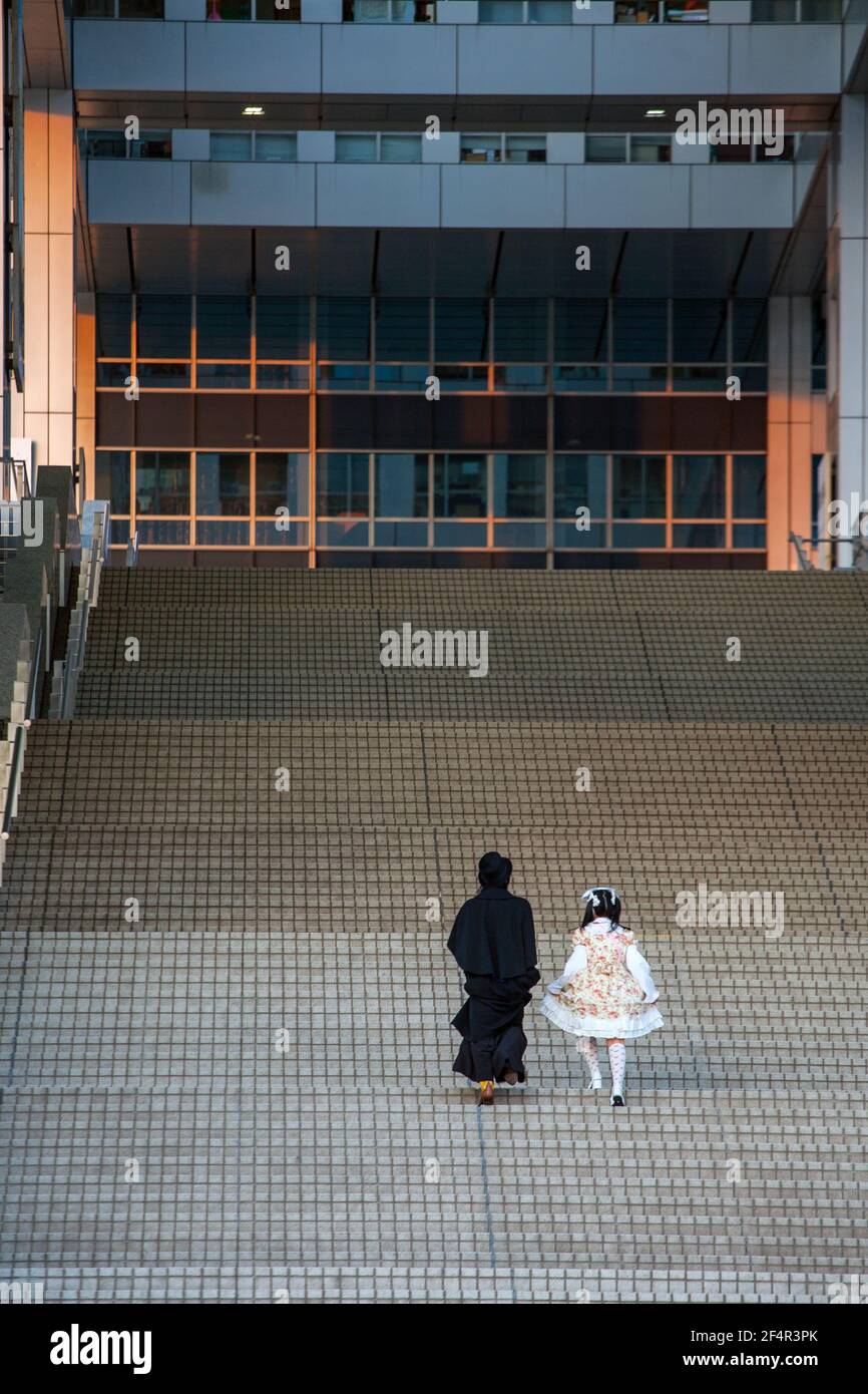 Vue arriere lointaine du couple japonais douce Lolita portant une robe rose jupon et homme en manteau de grenouille grimpant sur des marches abruptes a la baie de Tokyo Japon Photo