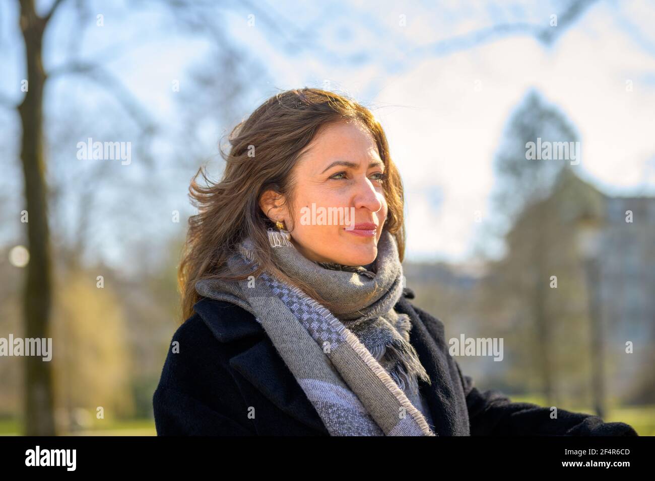 Belle femme d'âge moyen portant une écharpe chaude et un manteau relaxant à  l'extérieur, sous le soleil du printemps, assis sur un banc de parc une  tête et un épaulement rapprochés Photo
