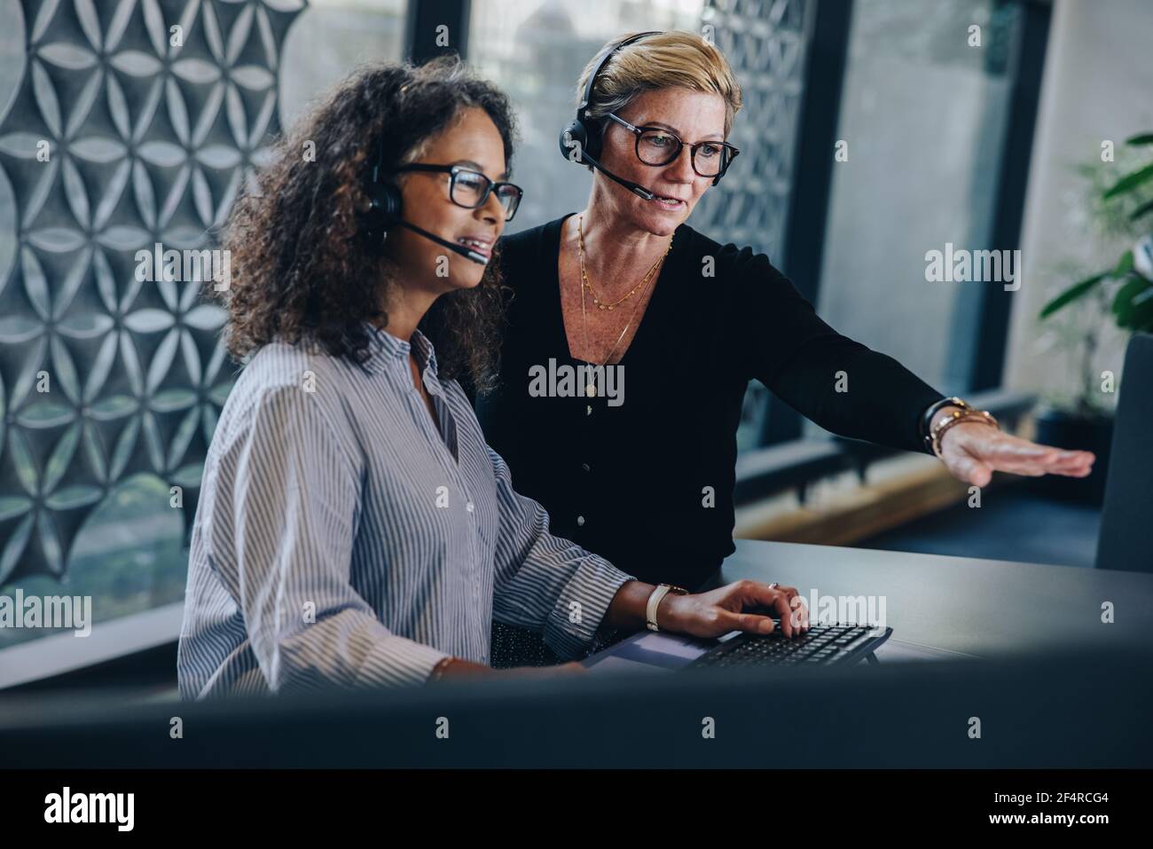 Deux femmes d'affaires portant un casque travaillant ensemble sur un ordinateur dans un centre d'appels. Femme professionnelle pointant vers l'écran d'ordinateur et discutant d'un problème Banque D'Images