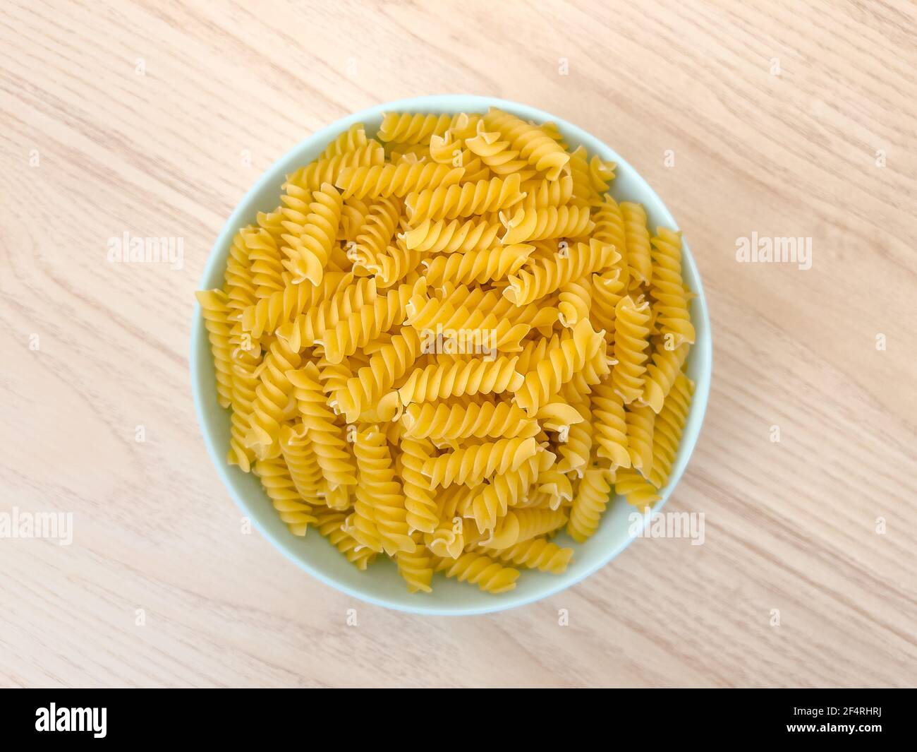 Pâtes italiennes sèches crues en forme de spirale dans un bol sur une table en bois dans la cuisine. La nourriture. Vue de dessus. Macaroni non cuit. Banque D'Images