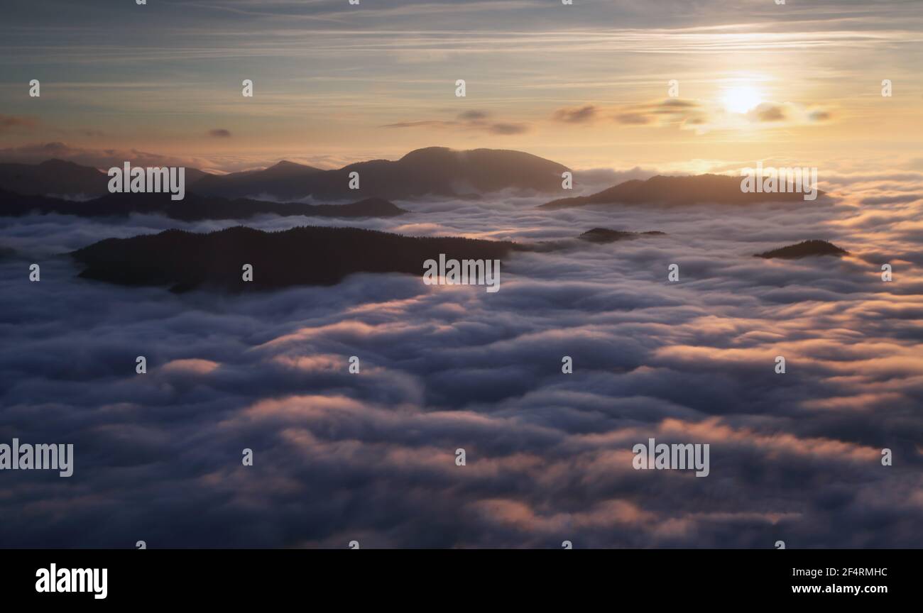 Coucher de soleil caché derrière les nuages et brouillard sur les collines, soleil jaune vif sur un paysage nuageux coloré, ciel bleu violet orange. Banque D'Images