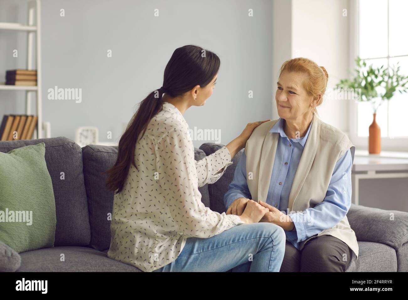 Bonne mère âgée et jeune fille assise sur le canapé, tenant les mains et parlant Banque D'Images