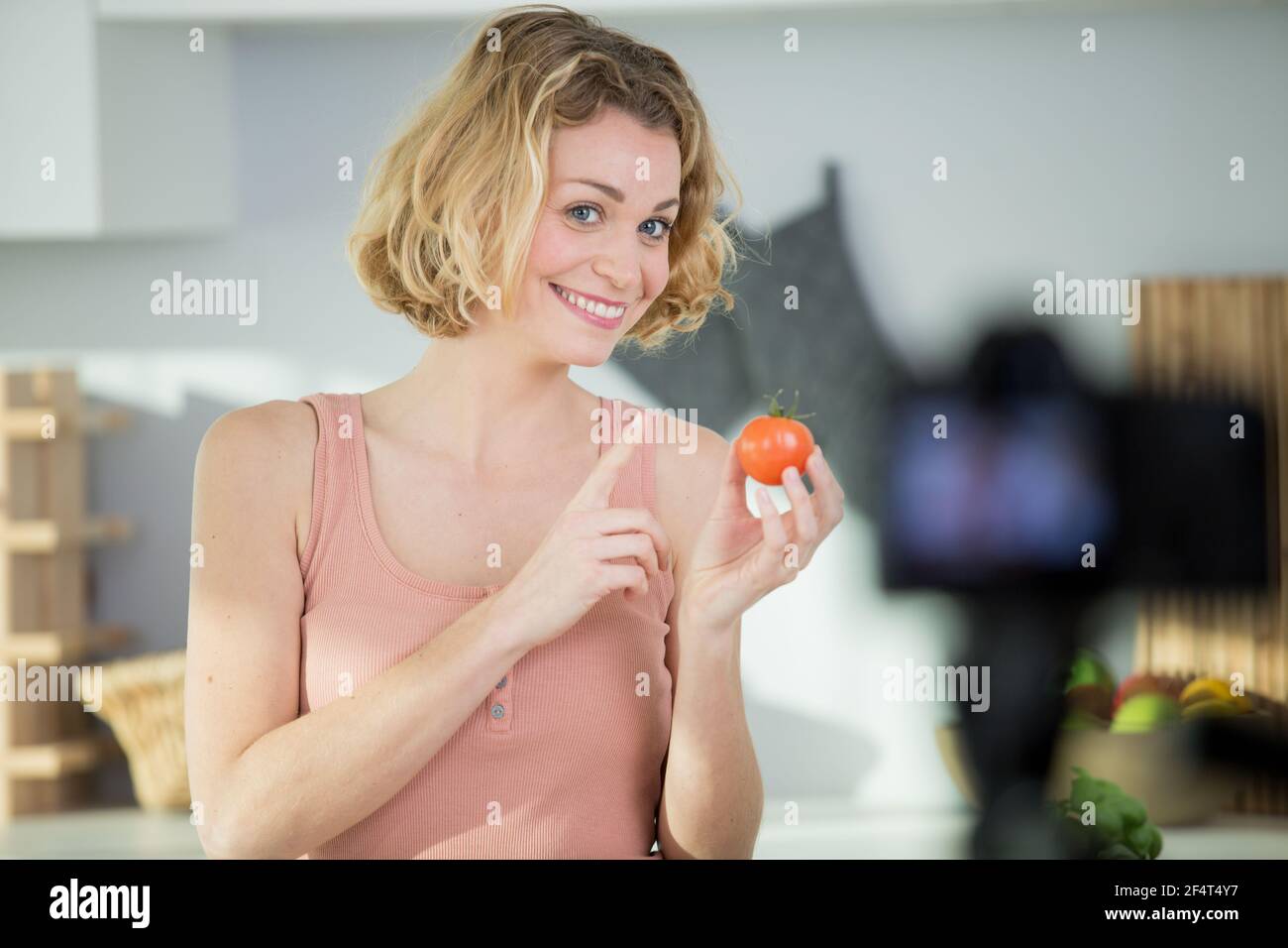 femme enregistrant un blog de cuisine tenant une tomate Banque D'Images