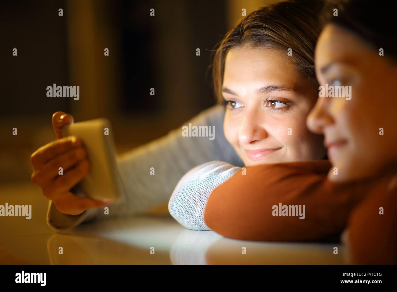 Deux amis regardent des fichiers multimédias sur leur smartphone sur un table dans la nuit à la maison Banque D'Images