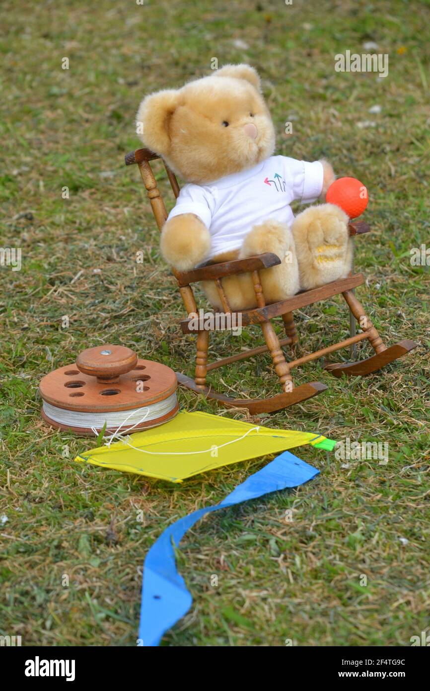 Petit ours en peluche assis sur UNE chaise à bascule avec UN Miniature jaune cerf-volant sur l'herbe verte - Festival du cerf-volant Banque D'Images