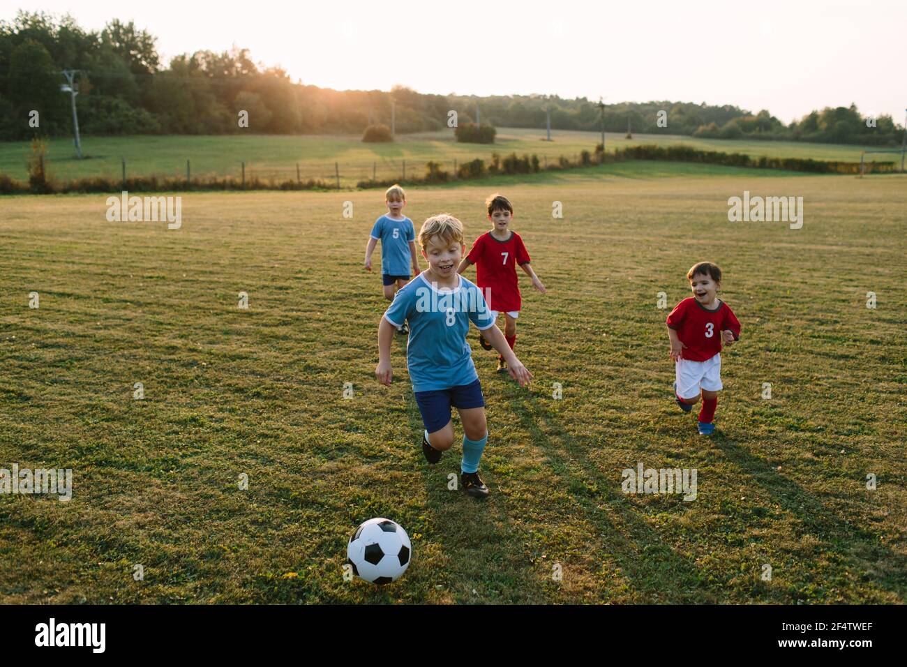 Enfants jouant au football. Des garçons gais dans des robes de football courant après le ballon sur le terrain. Banque D'Images