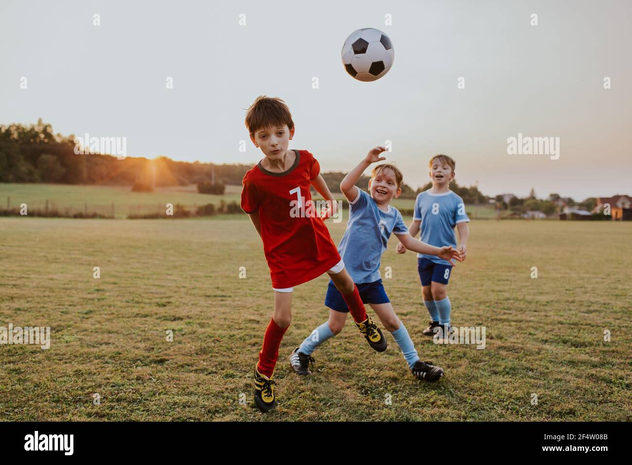 Enfants jouant au football amateur. Sur toute la longueur des jeunes garçons vêtues de robes de football ayant une tête de lit amusante sur le terrain. Banque D'Images