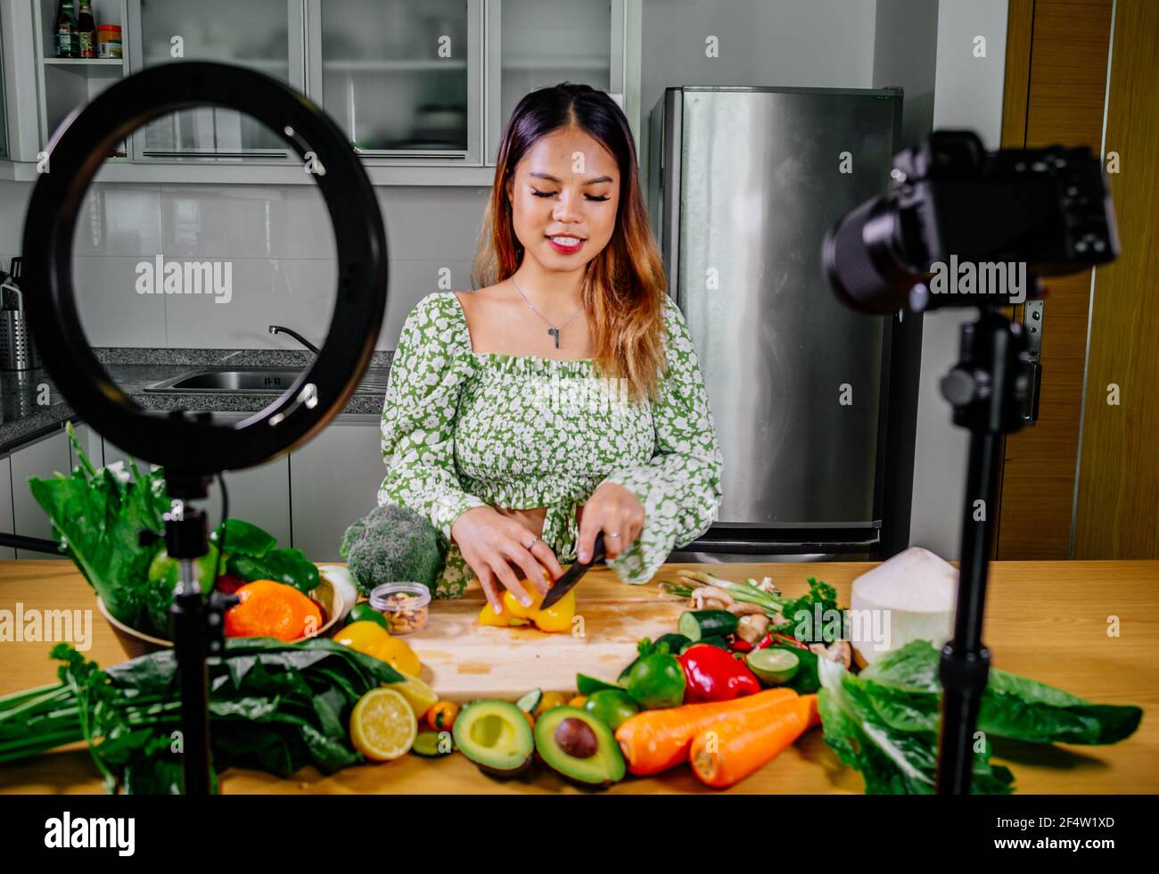 Femme asiatique blogueur ou créateur de contenu de cuisine et d'enregistrement caméra vidéo. Montrant la nourriture saine tout en enregistrant avec l'appareil photo dans la cuisine. Banque D'Images