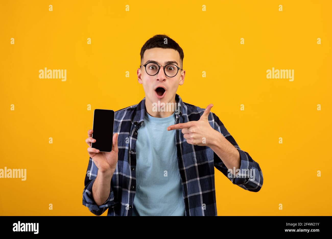 Jeune homme enthousiaste pointant vers un smartphone avec écran vide sur fond orange studio, espace pour la conception d'applications ou de sites Web Banque D'Images
