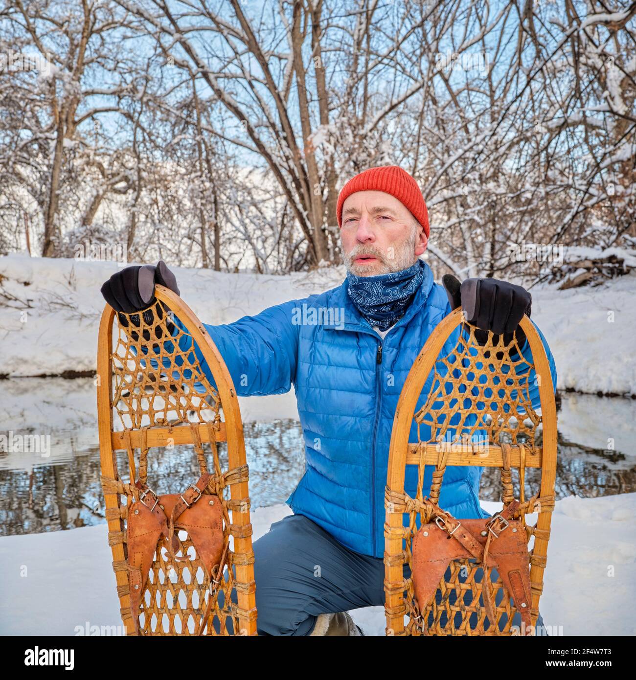 Homme âgé avec des raquettes en bois classiques (Bear Paw) sur une rive de ruisseau, paysage d'hiver au Colorado Banque D'Images